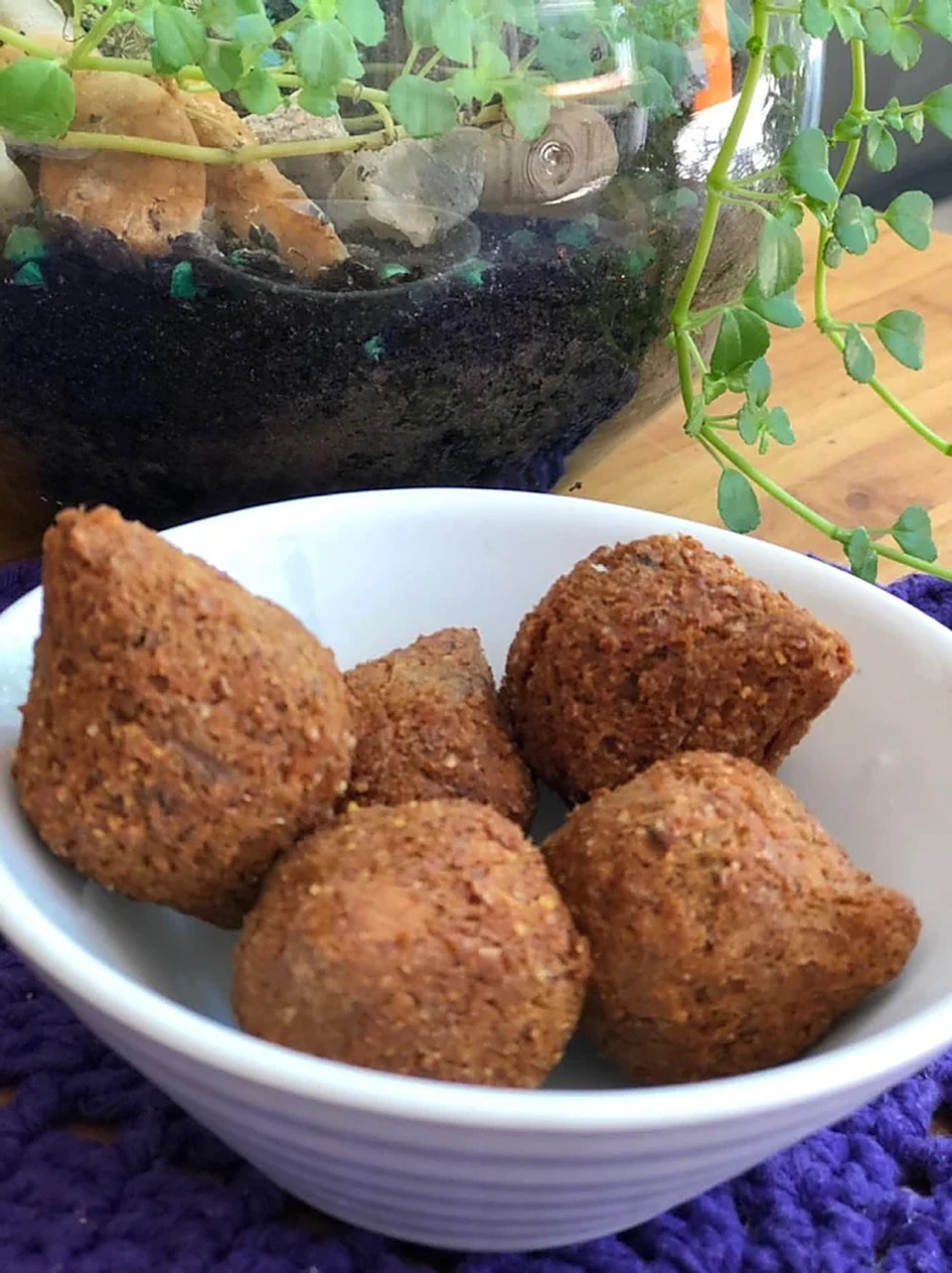 Quibes fritos servidos em tigela branca de louça sobre toalha de crochê roxa